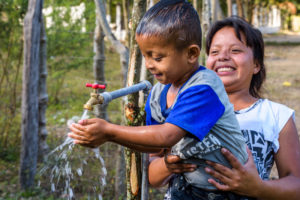 Johanna Hernandez, 23, holds her son David, 5, so he can wash his face and drink clean water flowing from one of the taps built by the community with funding from World Vision US. Photo credit: ©2019 World Vision, Jon Warren